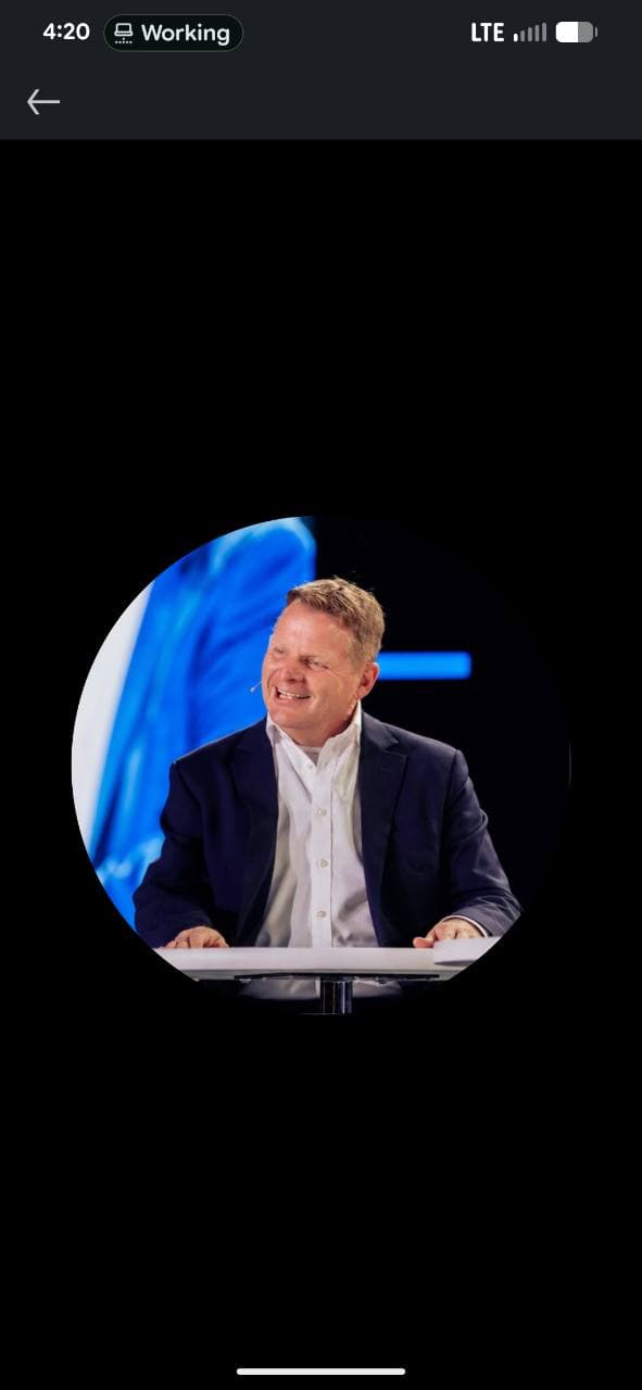 Tim Jacobs smiling while seated at a table, wearing a dark jacket and a headset microphone